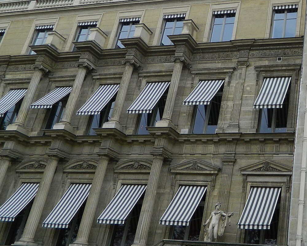 Striped awnings over tall windows on a stone building in Paris